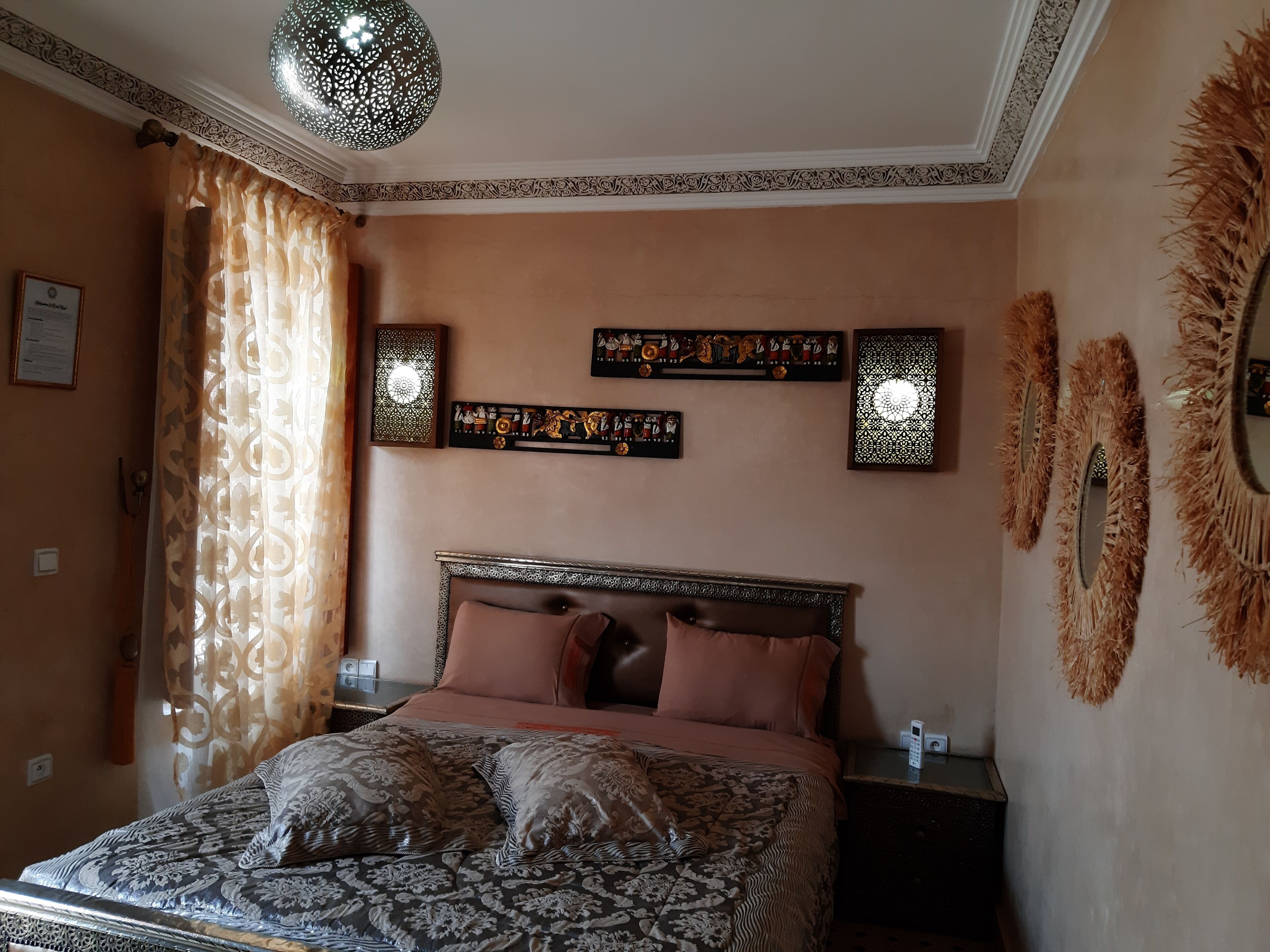 Un dormitorio con cama, ropa de cama estampada, decoración en la pared y una lámpara colgante.