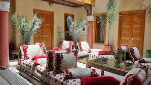 A traditional Moroccan interior with ornate wooden doors, a patterned sofa set, and potted plants. - Riad Miral (Marrakech)