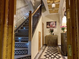 Una imponente escalera con baldosas blancas y negras en patrón, una pared decorativa con un cuadro enmarcado, y una alfombra estampada.