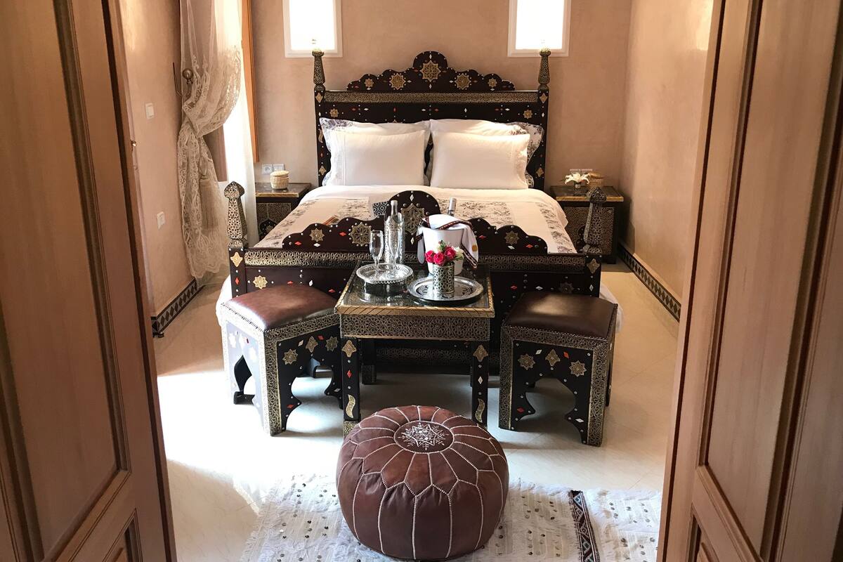 Ein traditionell eingerichteter Raum mit einem Bett, zwei Nachttischen, einem Tisch mit Tablett, einem dekorativen Hocker und einem gemusterten Teppich.