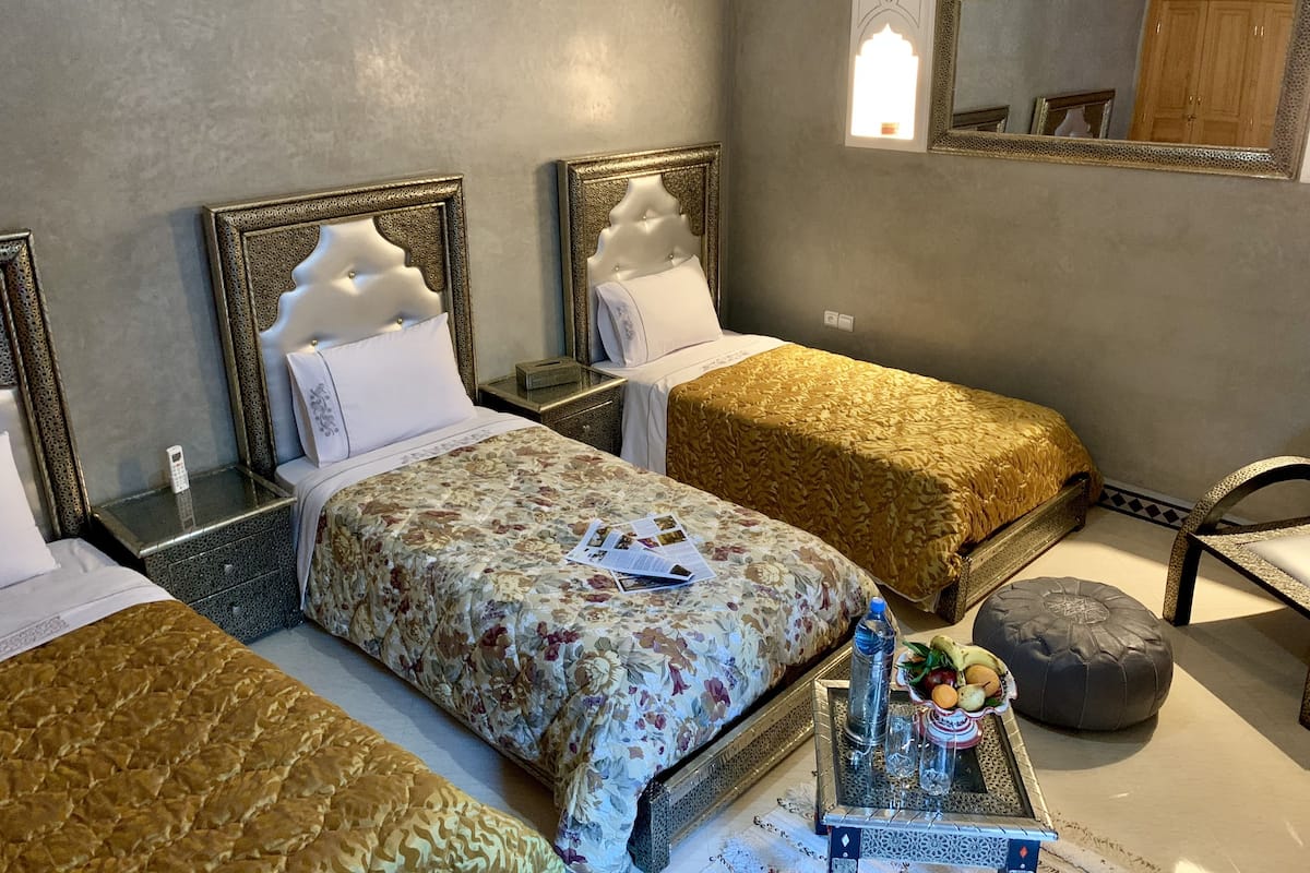 Ein Hotelzimmer mit zwei Betten, einem kleinen Tisch mit Flasche und Gläsern, einem Spiegel und einem Kleiderschrank.