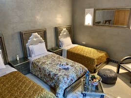 Habitación de hotel con dos camas, una mesita con una botella y vasos, un espejo y un armario.