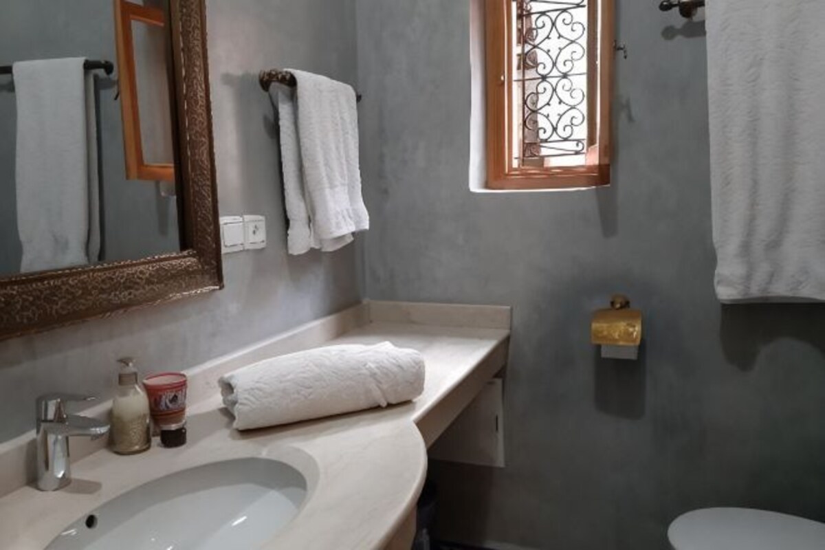 Un baño con un espejo grande, un lavamanos, una ventana y un inodoro.