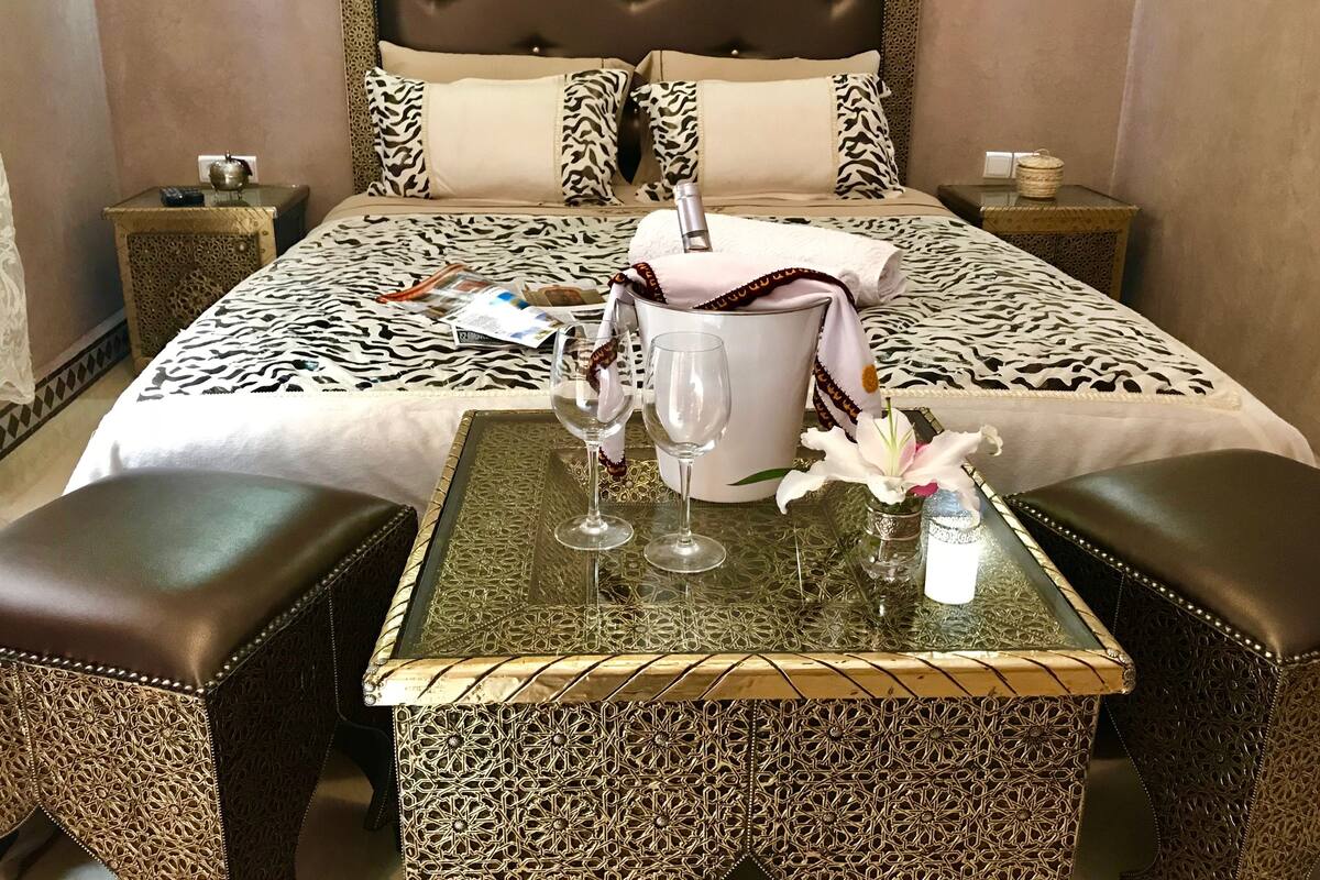 Ein Hotelzimmer mit einem Bett, zwei Nachttischen, einem Glastisch mit zwei Stühlen und einer Blumenvase als Dekoration.