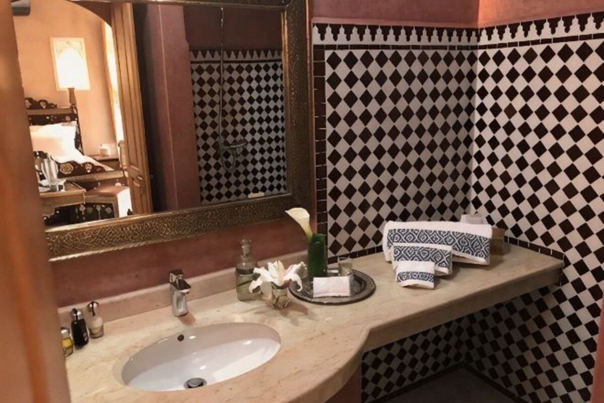 Un baño con lavamanos, espejo, artículos de aseo y azulejos estampados.