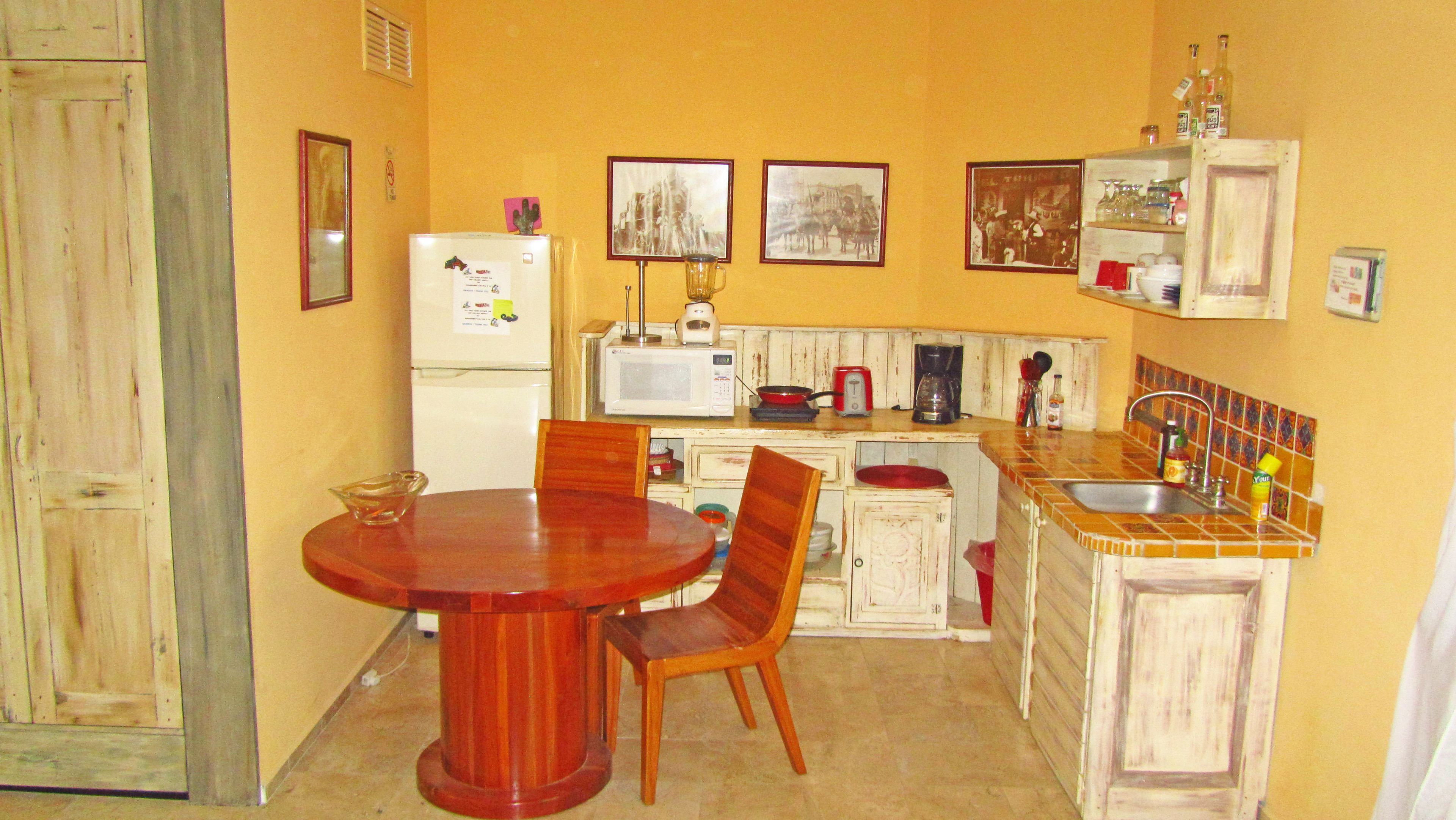 A compact kitchen with a dining table and chairs, a refrigerator, a microwave, a coffee maker, and a sink.
