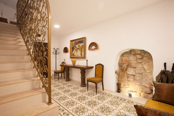 A staircase with ornate metal railings, a dining area with a table and chairs, a stone wall, and a decorative painting on the wall. - Vila Caelus Masia Boutique (Rubió)