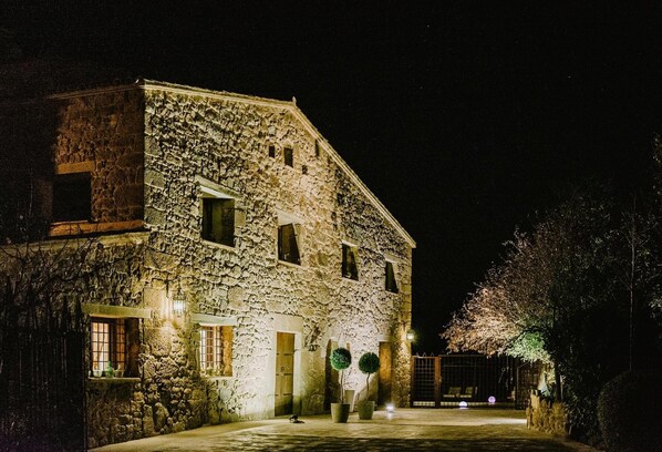 A stone building with multiple windows and a gated entrance at night. - Vila Caelus Masia Boutique (Rubió)