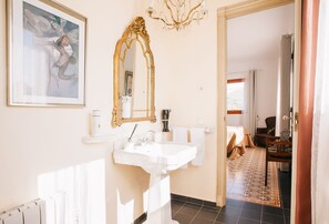 Un baño con lavamanos pedestal, un espejo grande y decorativo, y una obra de arte enmarcada en la pared.