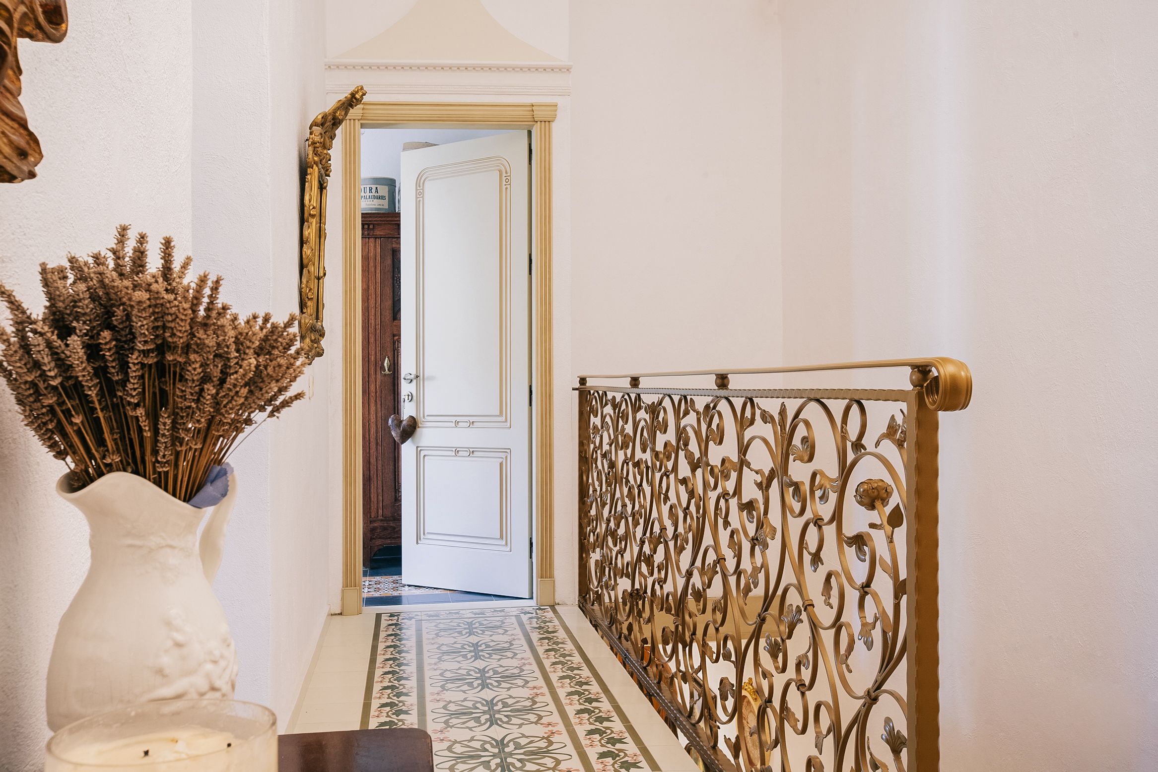 A hallway with a white door, a decorative metal railing, and a patterned floor.