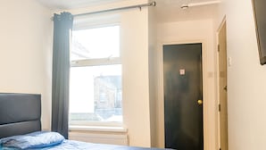 A bedroom with a bed, a window, a door, and a radiator. - La Tavola Calda Hotel (Nuneaton)