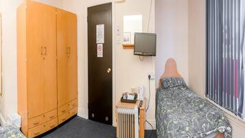Un dormitorio con cama, armario, radiador, televisor y ventana con persianas.