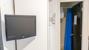 A room with a mounted television, a door leading to a bathroom with a blue shower curtain, and a white towel hanging on the door. - La Tavola Calda Hotel (Nuneaton)