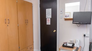 A hotel room with a wardrobe, a door with a notice, a television, and a radiator. - La Tavola Calda Hotel (Nuneaton)