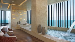 A modern interior with a wooden floor, a seating area with wicker furniture, a water feature, and a view of the ocean through large windows. - Hyatt Vivid Cancun Adults Only - All Inclusive  (Cancun)