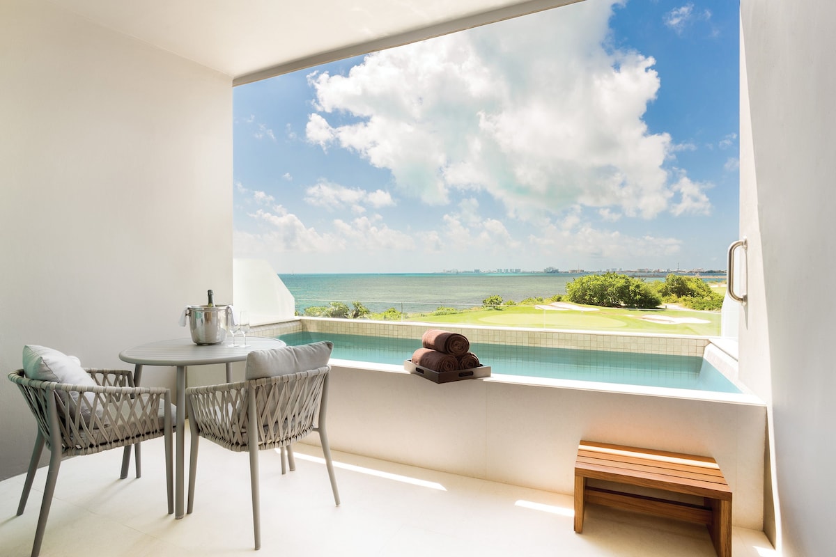 A balcony with a view of the sea, a pool, and a golf course.