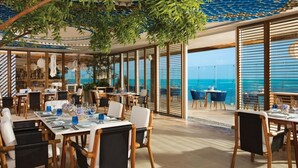 A restaurant with tables set for dining, large windows offering ocean views, and a ceiling with a blue patterned design. - Hyatt Vivid Cancun Adults Only - All Inclusive  (Cancun)