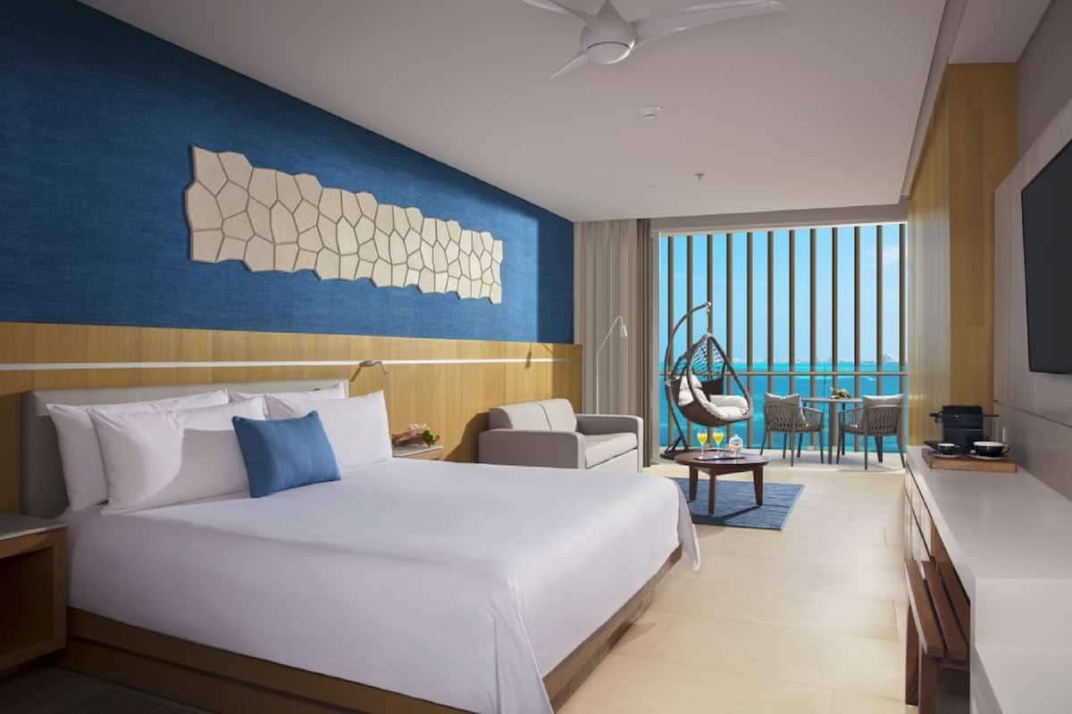 A hotel room with a large bed, a desk, a chair, and a view of the ocean.
