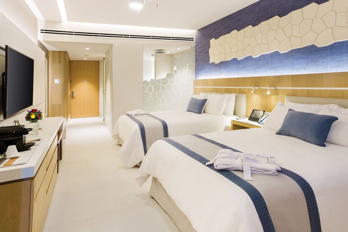 A hotel room with two beds, a desk, a TV, and a bathroom.