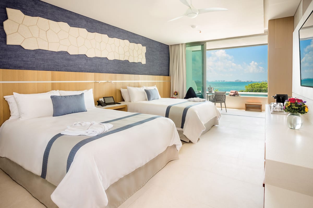 A hotel room with two beds, a desk, a chair, a view of the sea, and a balcony.