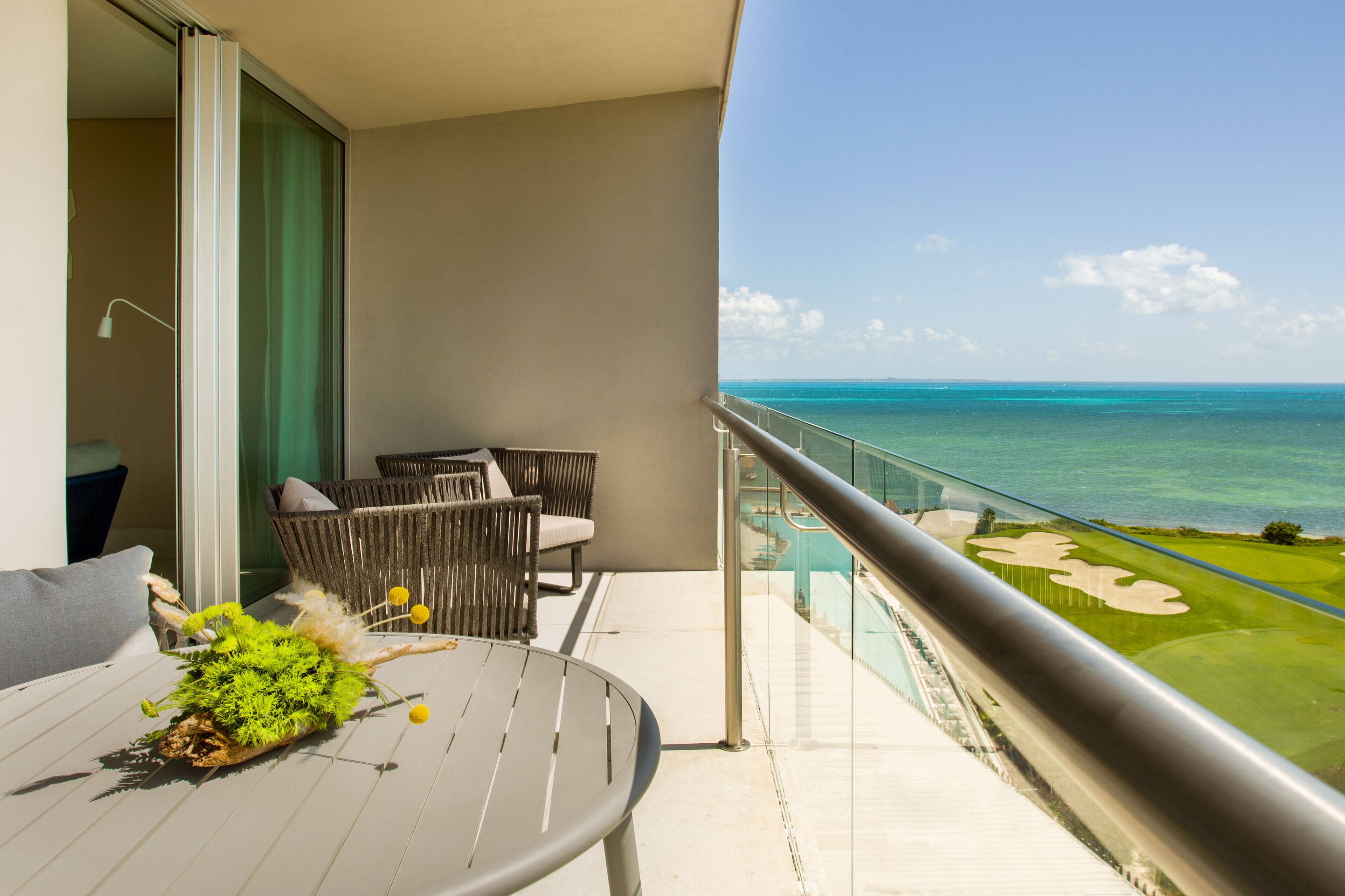 Ein Balkon mit Blick auf das Meer, ein Tisch mit einer Pflanze und eine Sitzgelegenheit mit Stühlen.