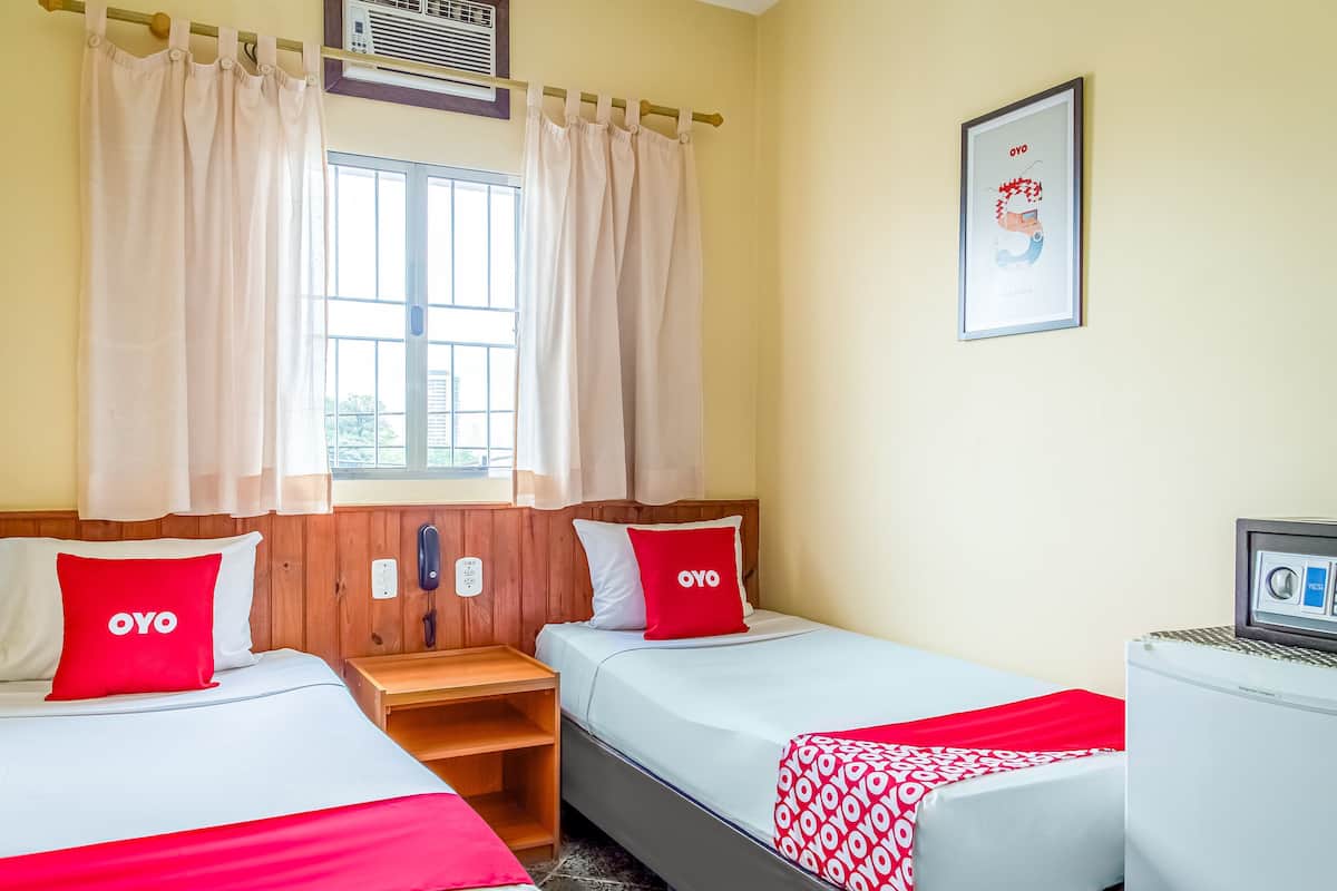 A hotel room with two beds, a wooden nightstand, a desk, and a window with curtains.