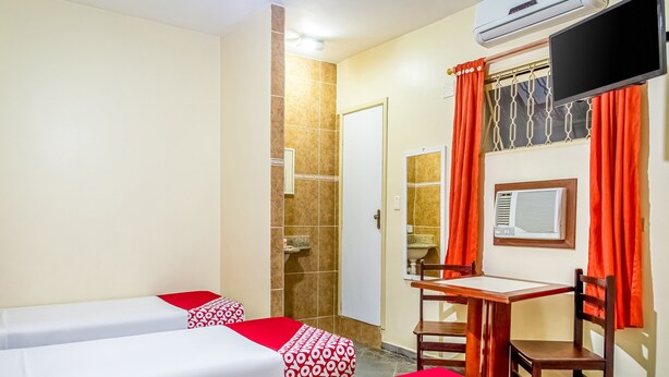 Habitación de hotel con dos camas, un escritorio, una silla, un equipo de aire acondicionado y un televisor.