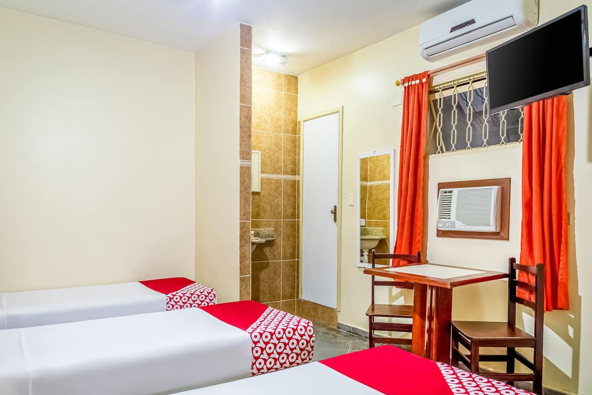 A hotel room with two beds, a desk, a chair, an air conditioning unit, and a television.