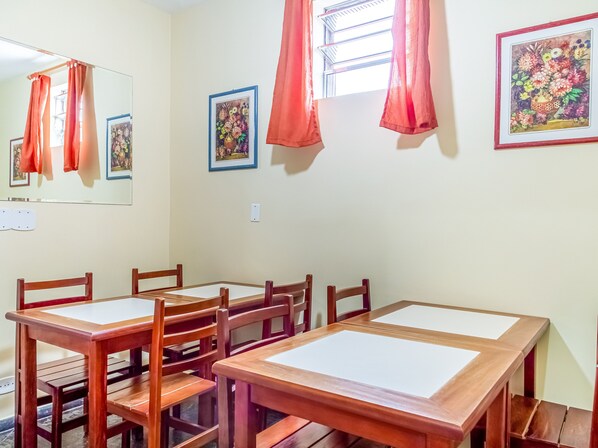 A dining area with wooden tables and chairs, framed floral artwork on the walls, and a window with curtains. - Hotel Macuco (São Paulo)