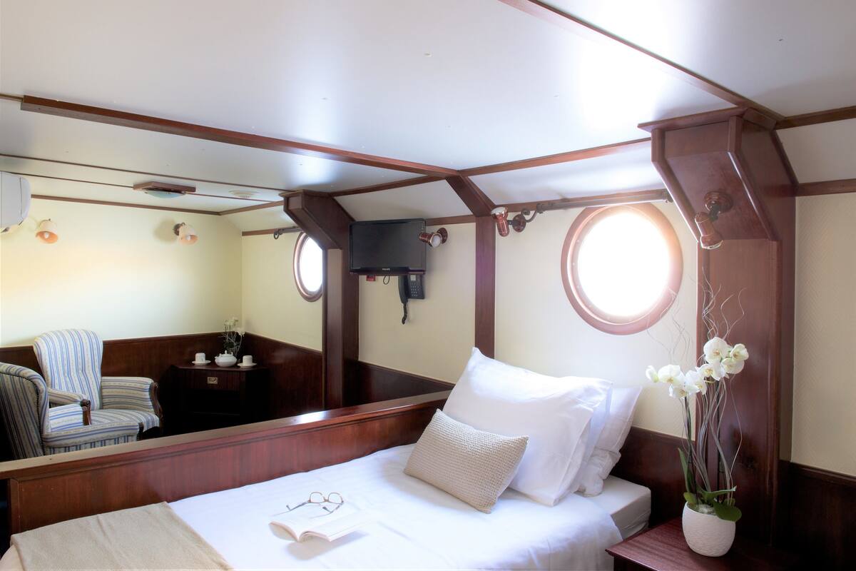 Un dormitorio con una cama de madera, una mesita de noche con un jarrón de flores, una silla y una ventana.