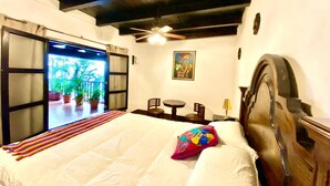 Une chambre à coucher avec un lit, un ventilateur de plafond, un tableau et une vue sur un jardin, visible à travers une porte coulissante.