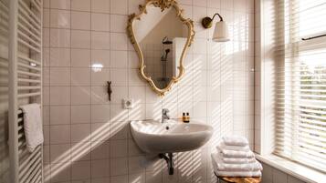 A bathroom with a white sink, a gold-framed mirror, a towel rack, and a window with blinds.