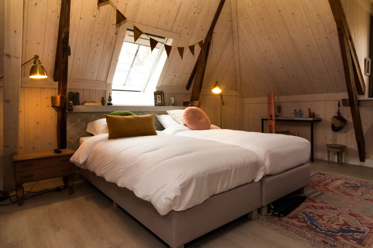A cozy bedroom with a large bed, wooden walls, and a sloped ceiling.