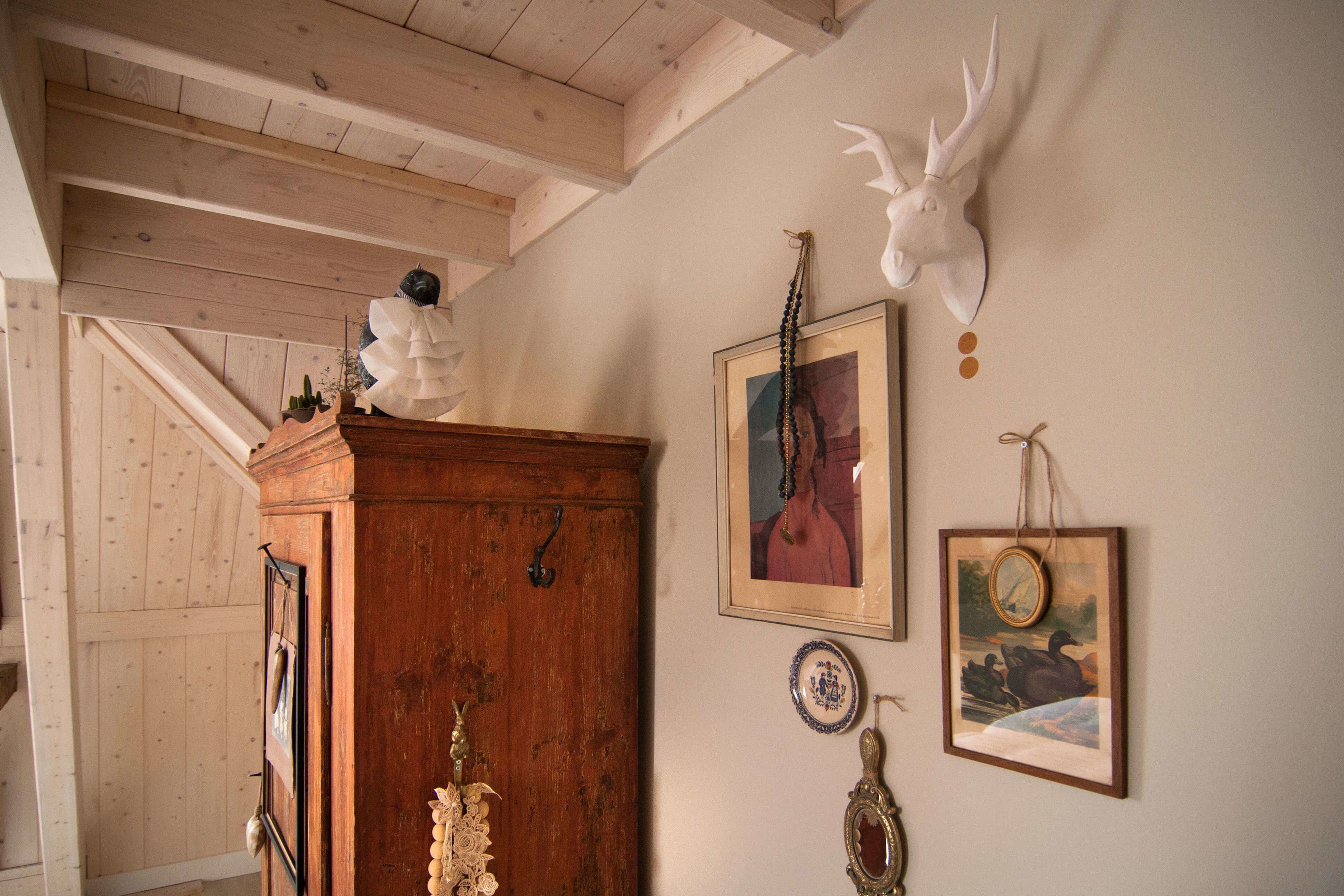 A rustic room with wooden beams, a wooden cabinet, and wall-mounted decorations including a deer head and framed artwork.