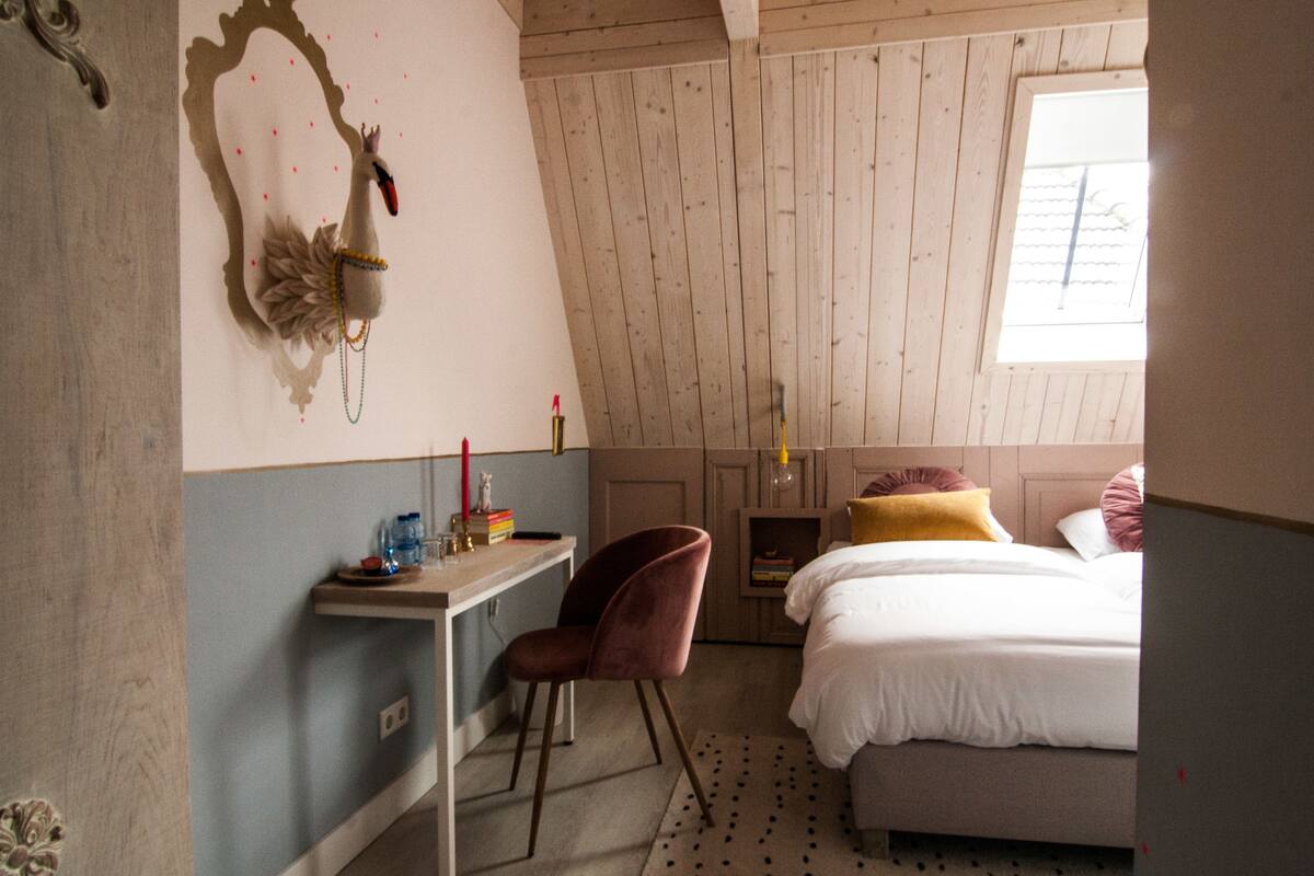 A bedroom with a bed, a desk, a chair, a mirror, and a window.