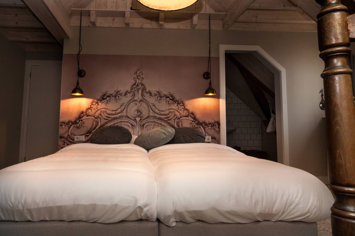 A double bed with white bedding, a decorative headboard, and two wall-mounted lamps.