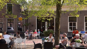 Um café ao ar livre com mesas e cadeiras, um edifício de tijolos ao fundo e pessoas a jantar.