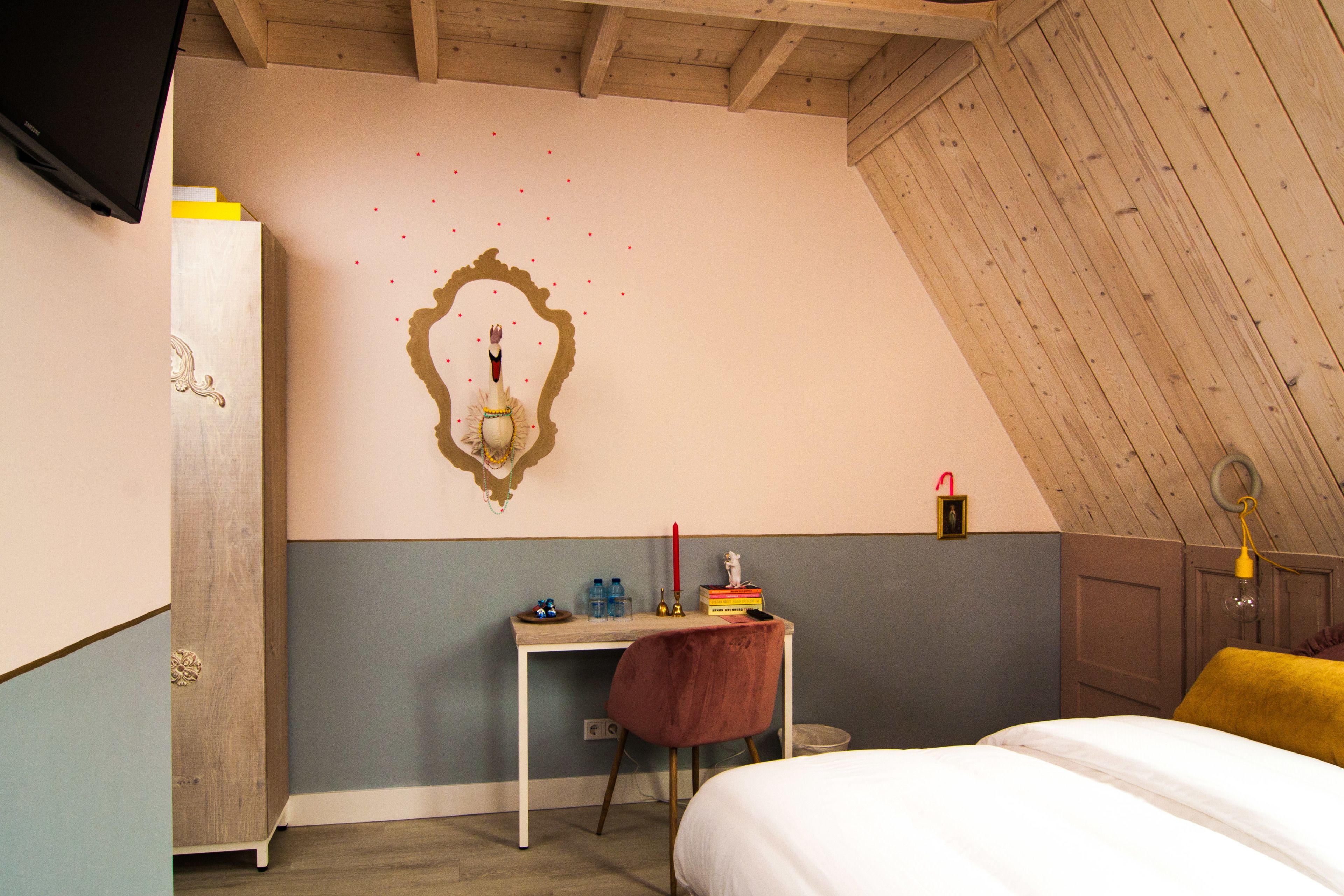 A bedroom with a sloped ceiling, a desk with a chair, a bed, and a wall-mounted mirror.