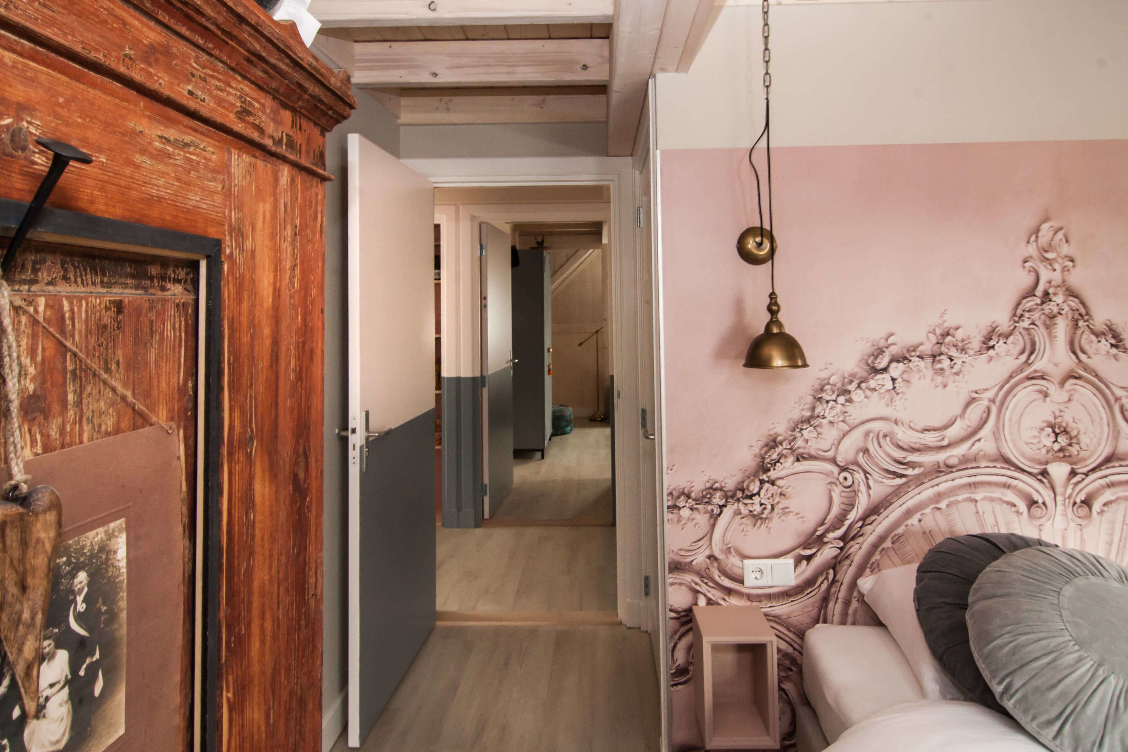 A bedroom with a wooden wardrobe, a bed with a decorative headboard, and a hallway leading to another room.