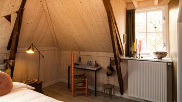 Ein gemütliches Schlafzimmer im Dachgeschoss mit schrägen Wänden, einem Holztisch, einem Stuhl, einem kleinen Hocker und einer Heizung.