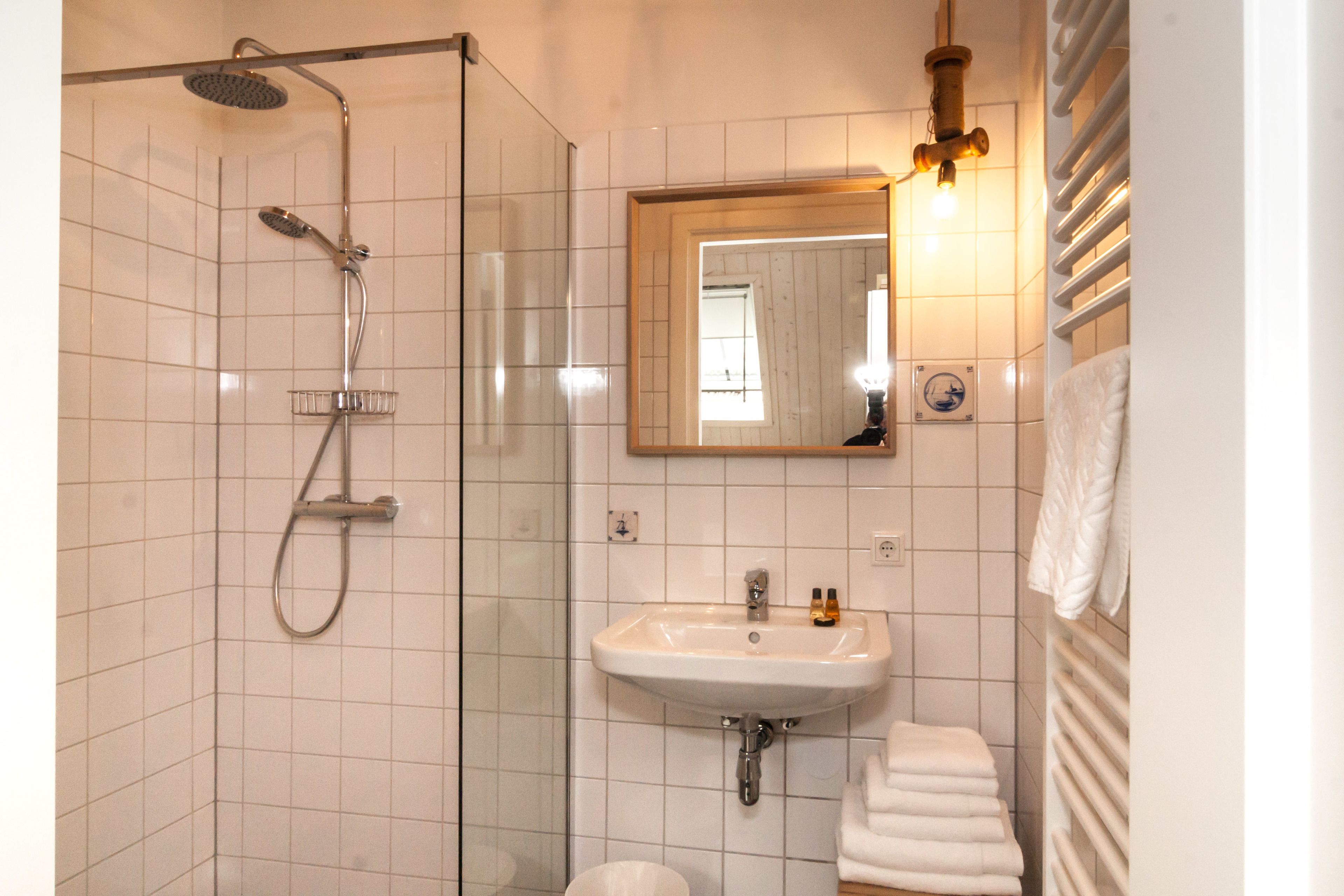 Een badkamer met een douche, wastafel en spiegel.