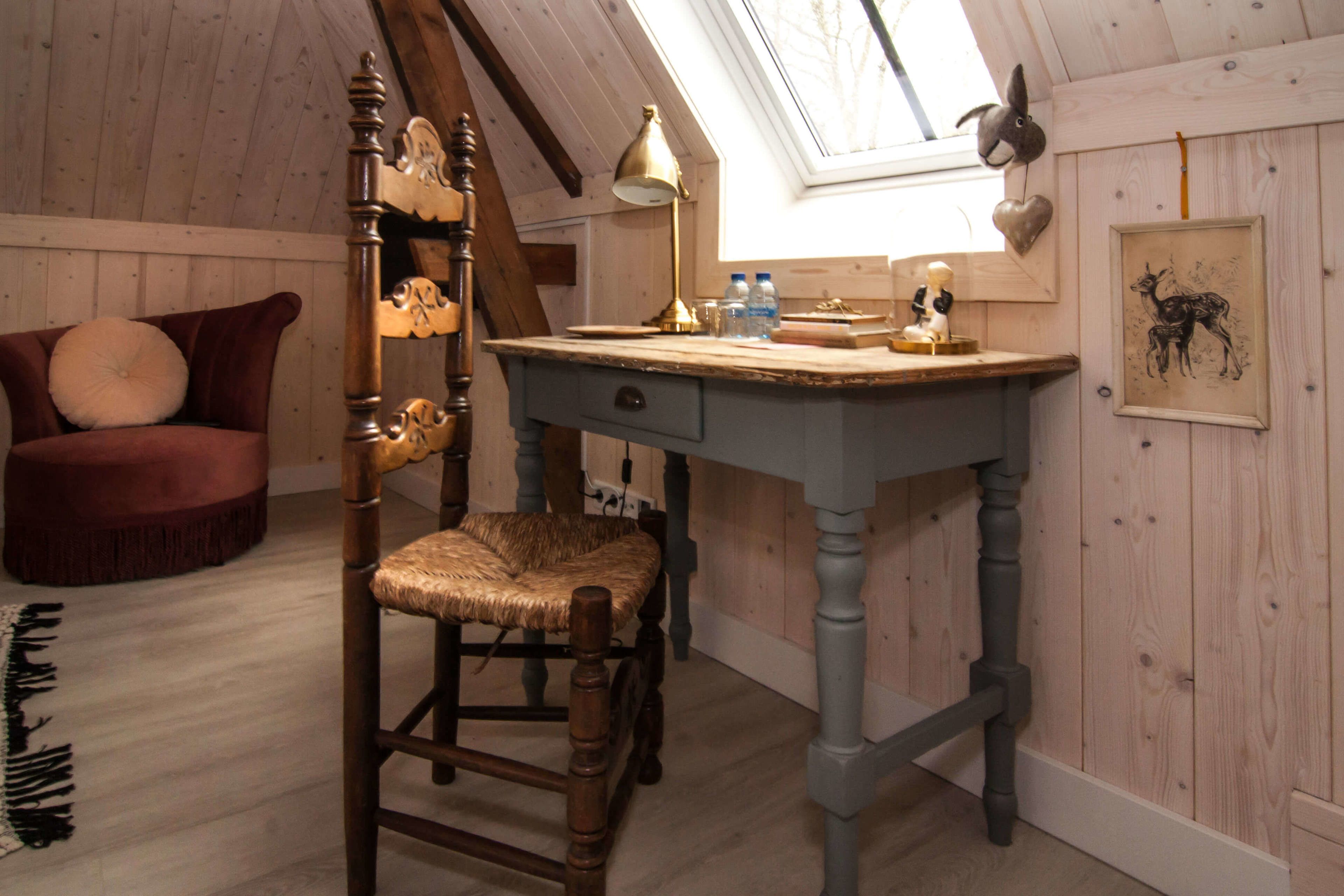 Een gezellige kamer met een houten bureau, een stoel, een lamp en een ingelijst beeld op de muur.