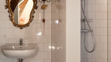 A bathroom with a white tiled wall, a white sink, a mirror with an ornate frame, a shower with a handheld showerhead, and a towel rack.
