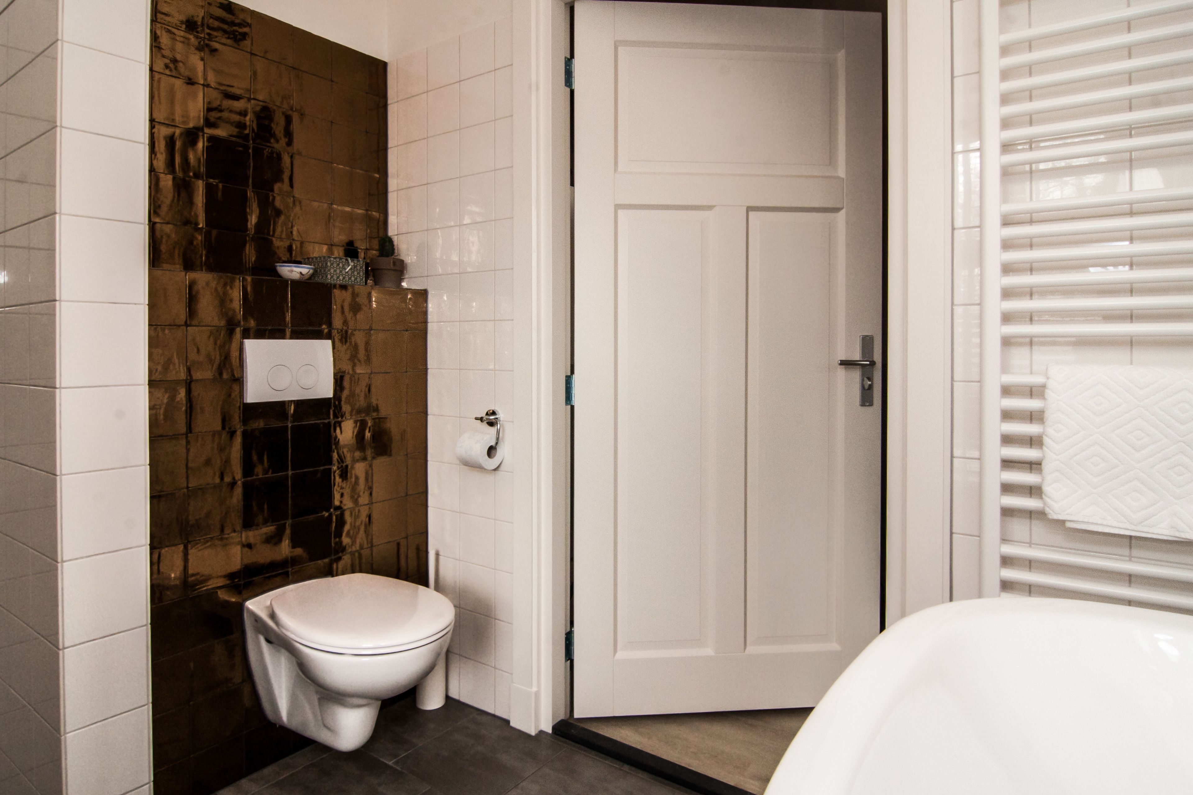 Een badkamer met een toilet, een witte deur en een handdoek aan een rek.