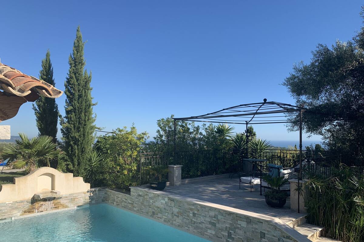 A swimming pool with stone tiles, surrounded by greenery and a pergola.