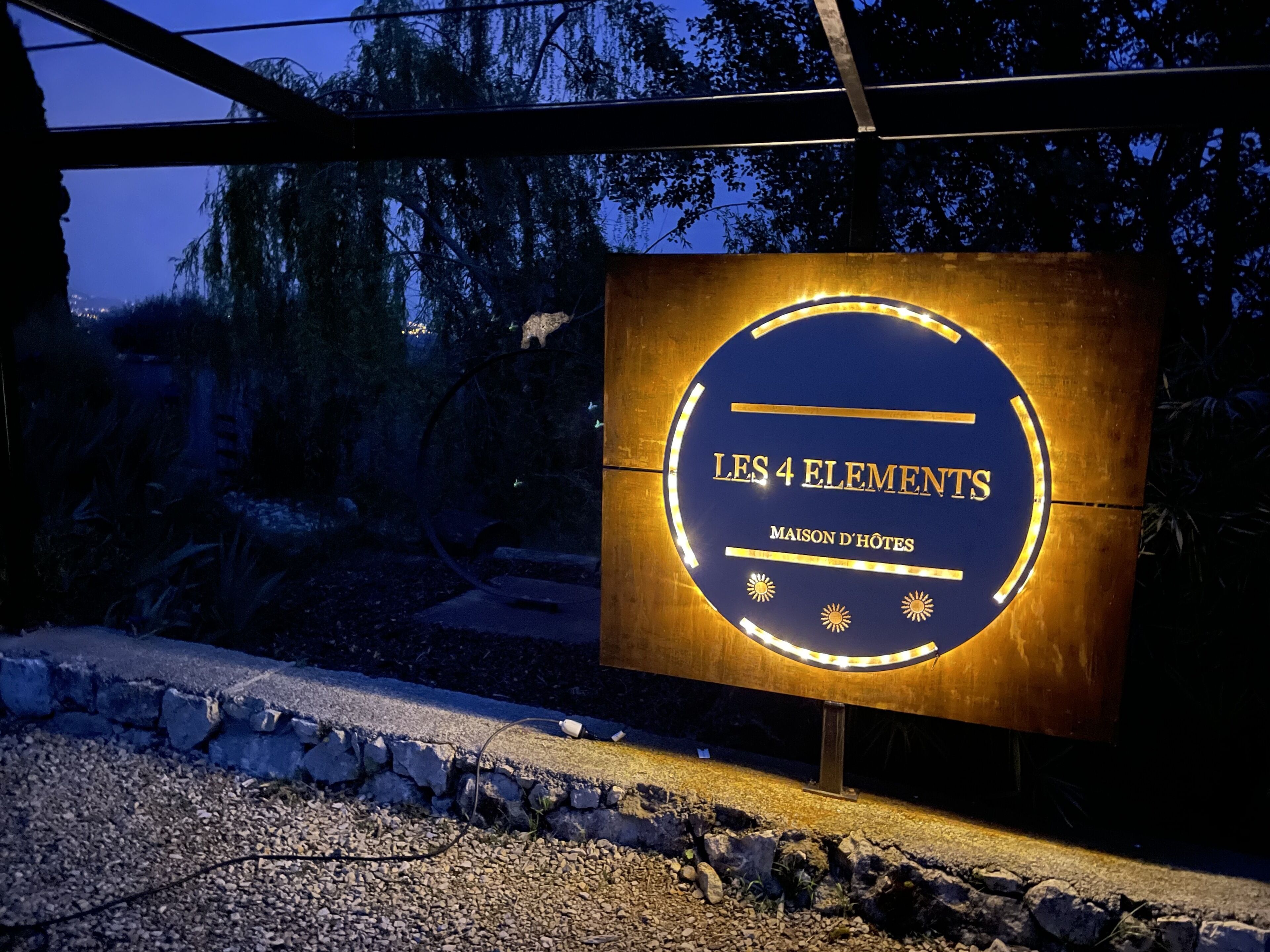 A sign for "LES 4 ELEMENTS MAISON D'HÔTES" with a circular design and illuminated edges.
