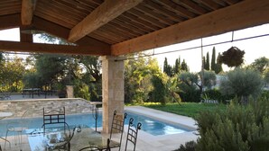 A covered outdoor area with a pool, stone pillars, and wicker chairs around a glass table. - Les 4 éléments (Tourrettes-sur-Loup)