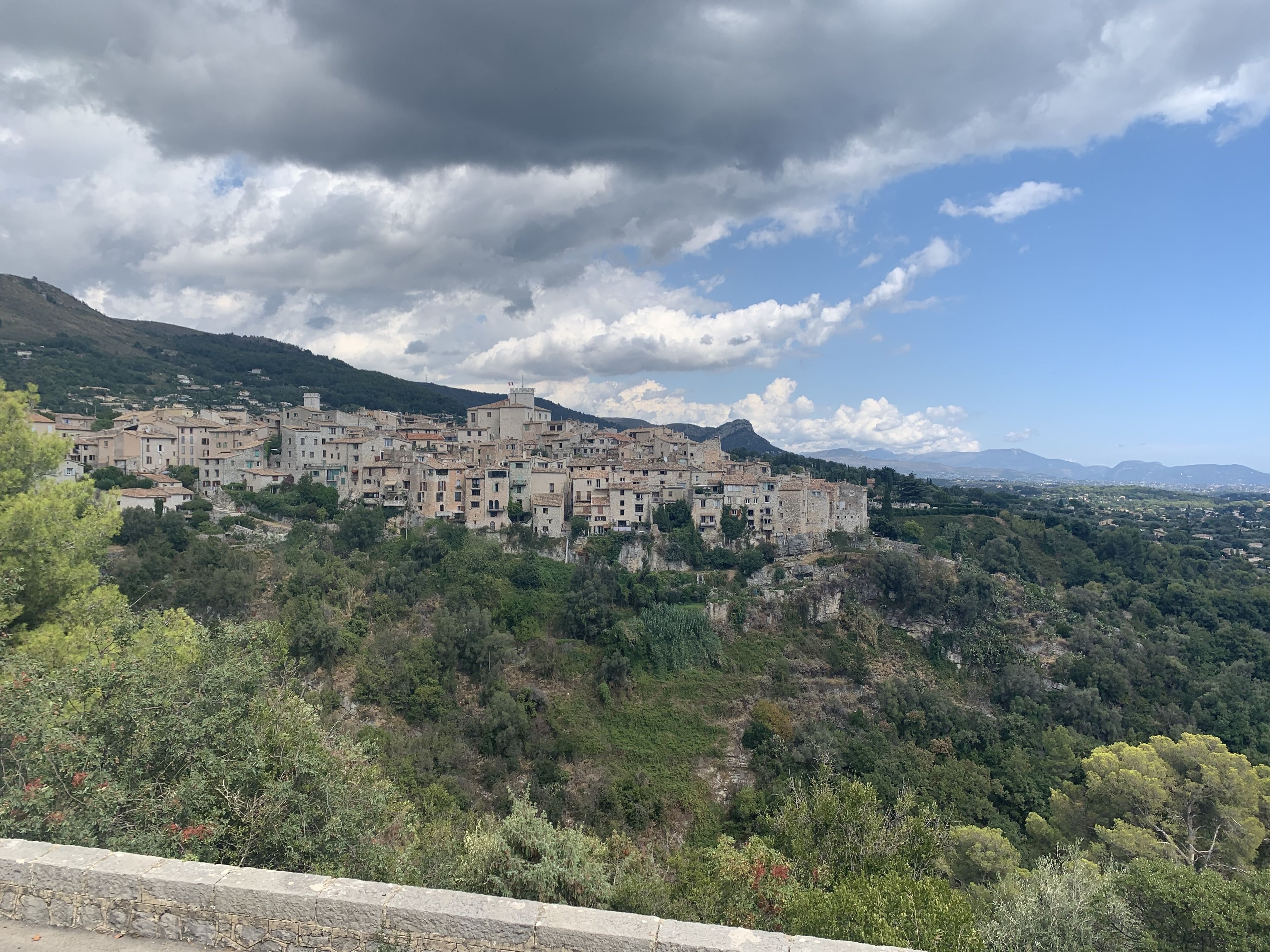 A historic town built on a hillside with traditional architecture, surrounded by lush greenery and mountains in the background.