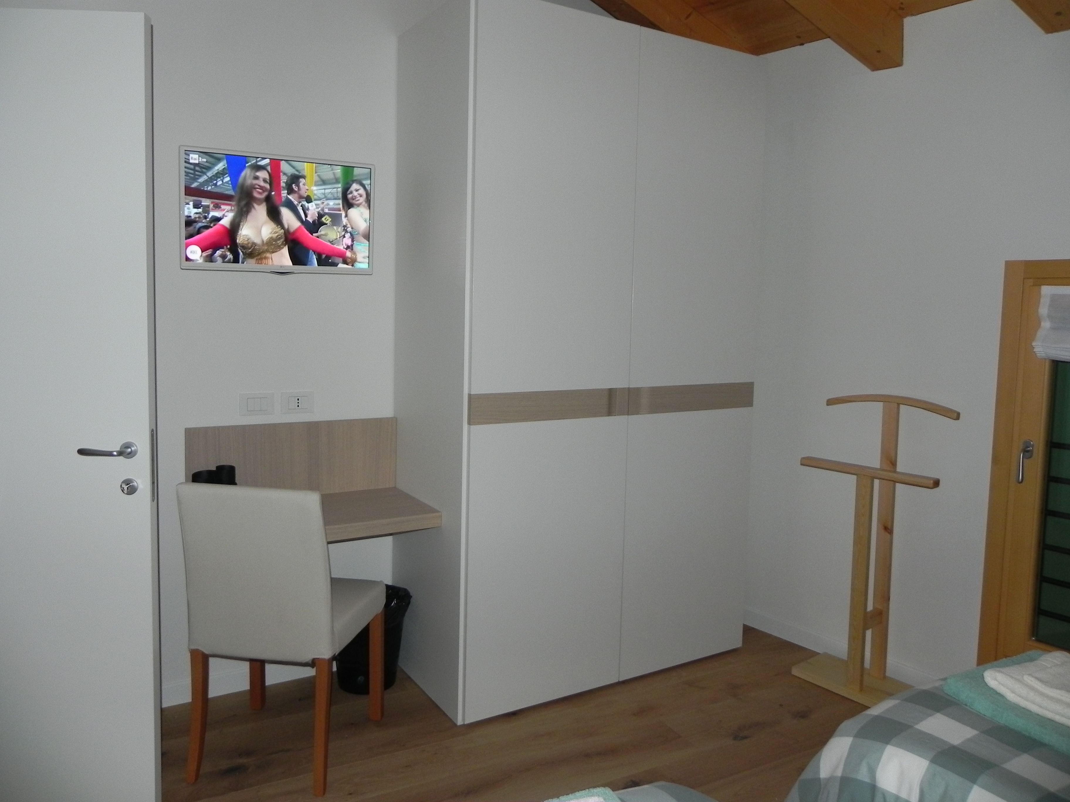 A bedroom with a bed, a desk, a chair, a TV mounted on the wall, and a wardrobe.