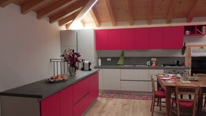A kitchen with red cabinets, a wooden dining table, and a black countertop. - da Meri Locazione Turistica Appartamento (Farra di Soligo)
